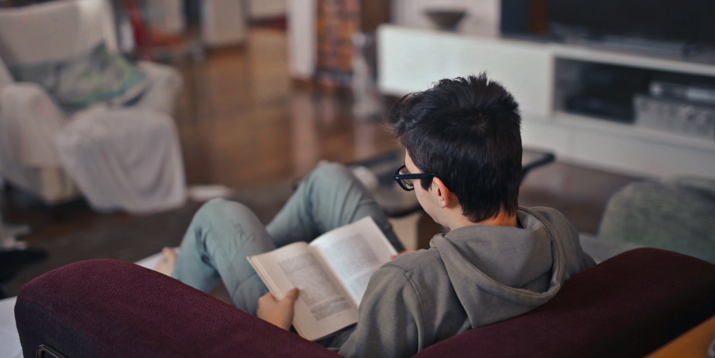 young man with glasses sitting on a comfy couch and reading a book