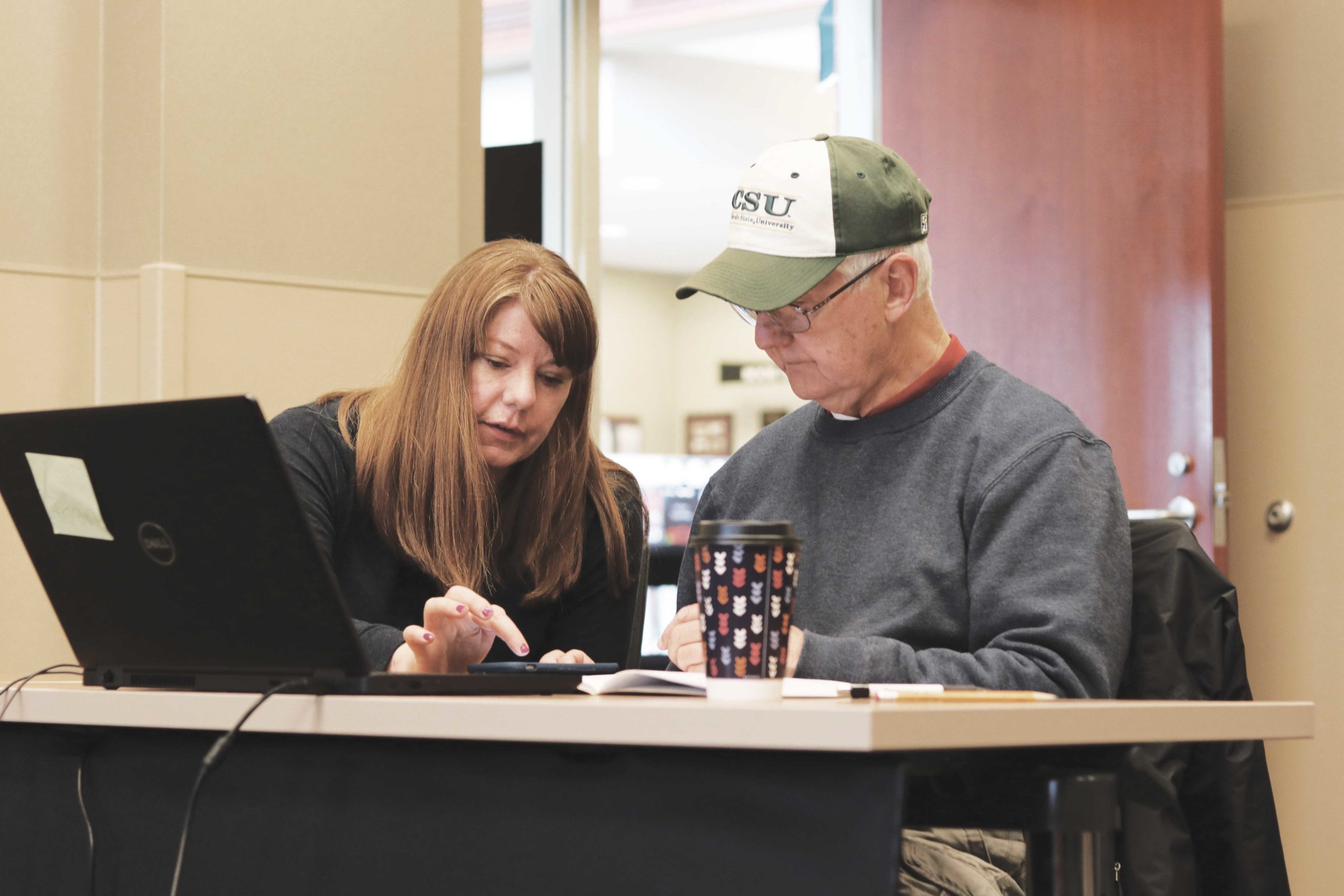 Librarian assisting patron with laptop and mobile device