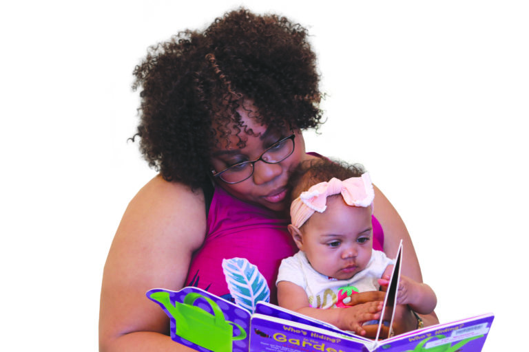 Parent holding baby in lap and reading a board book