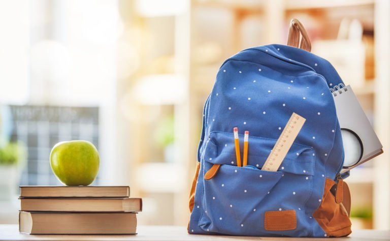 A pile of books with an apple on top next to a backpack