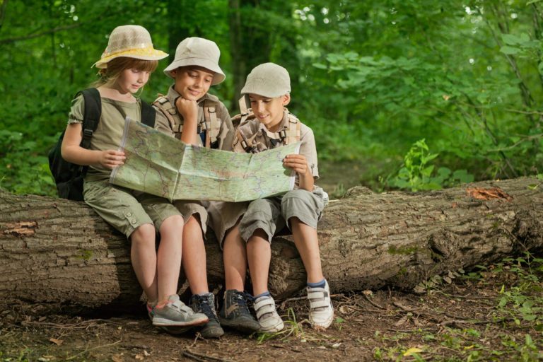 Three children sitting on a log in the forest, looking at a map
