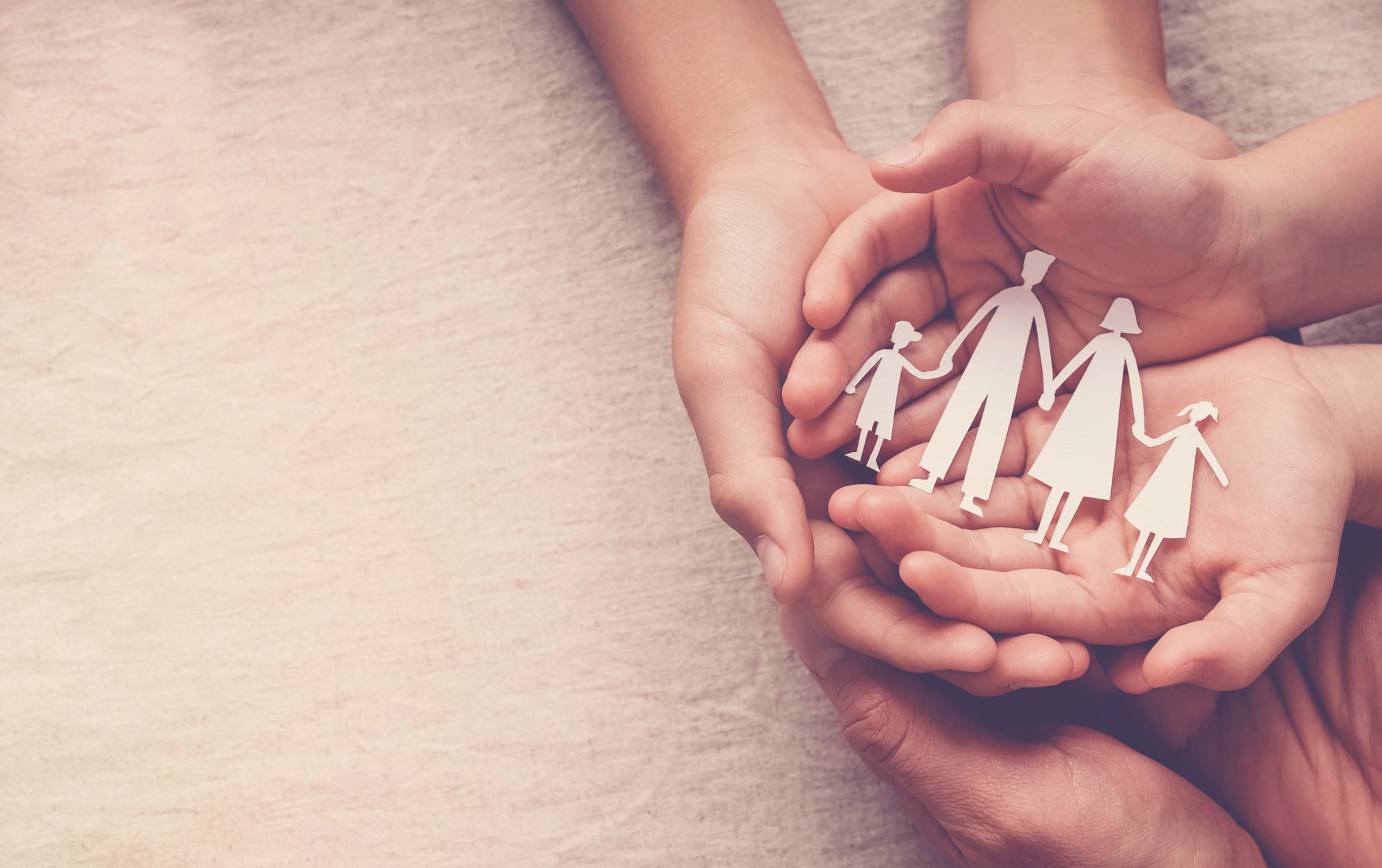Two pairs of hands holding a paper cutout of a family