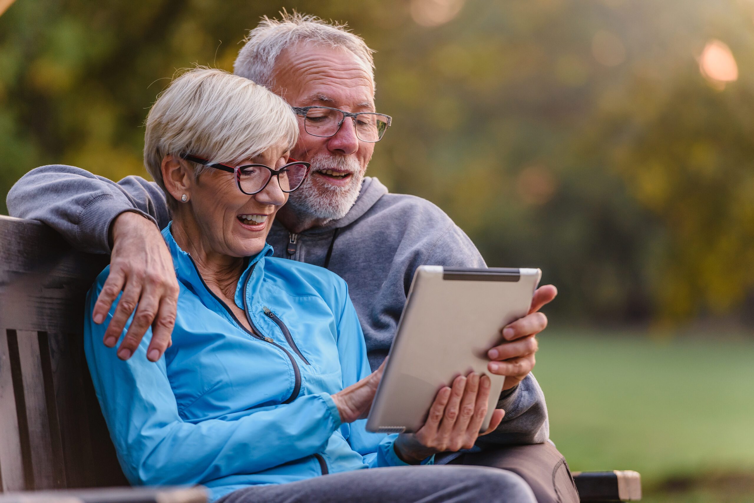 Smiling senior couple sitting on a bench looking at tablet