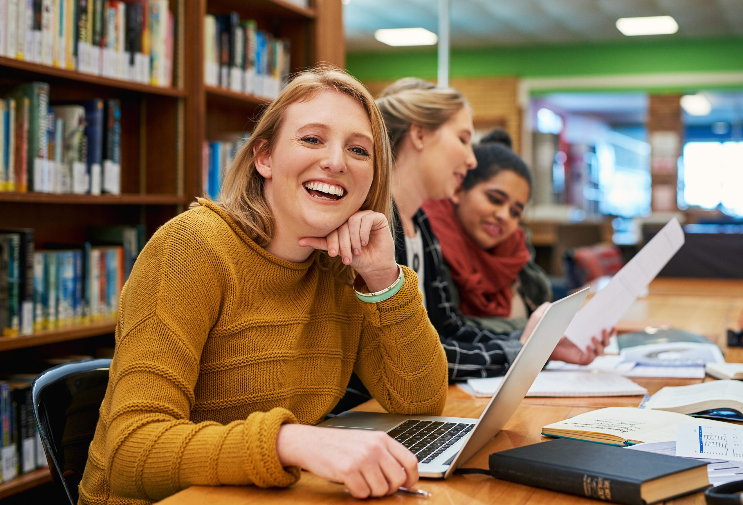 Happy young women studying in a library with papers and laptops