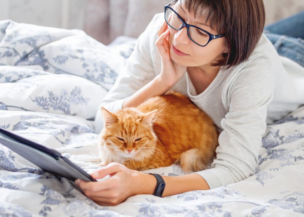 Woman with glasses reading tablet and cuddling orange cat