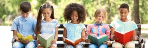 Diverse children reading on bench outside, happy