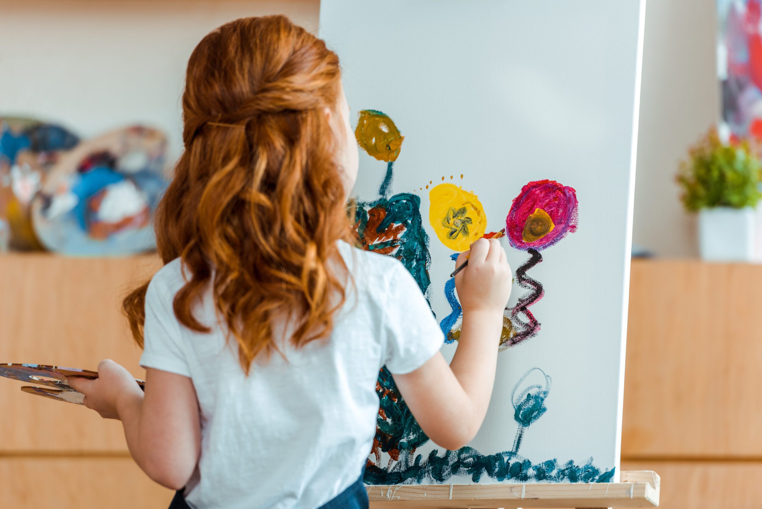 Back view of young girl painting on canvas.