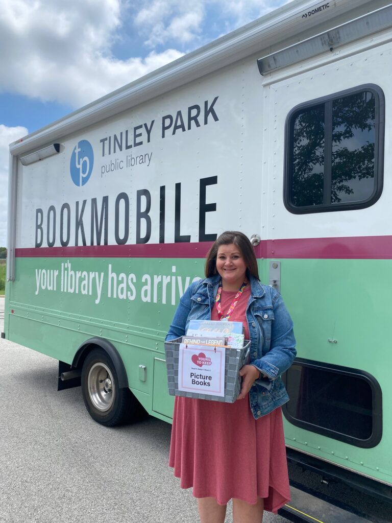 Library Staff member holding one of the "Yours to Keep" boxes in front of the bookmobile