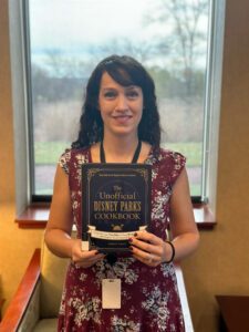 Library staff member holding up the cookbook "The Unofficial Disney Parks Cookbook" by Ashley Craft