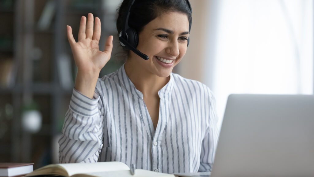 Woman smiling and waving at laptop during virtual job interview