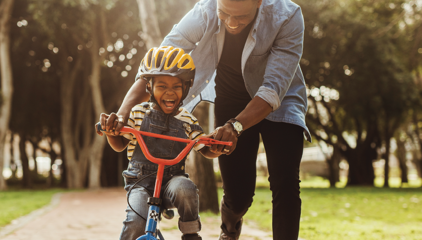 Laughing child learning to ride a bike, guided by their smiling parent