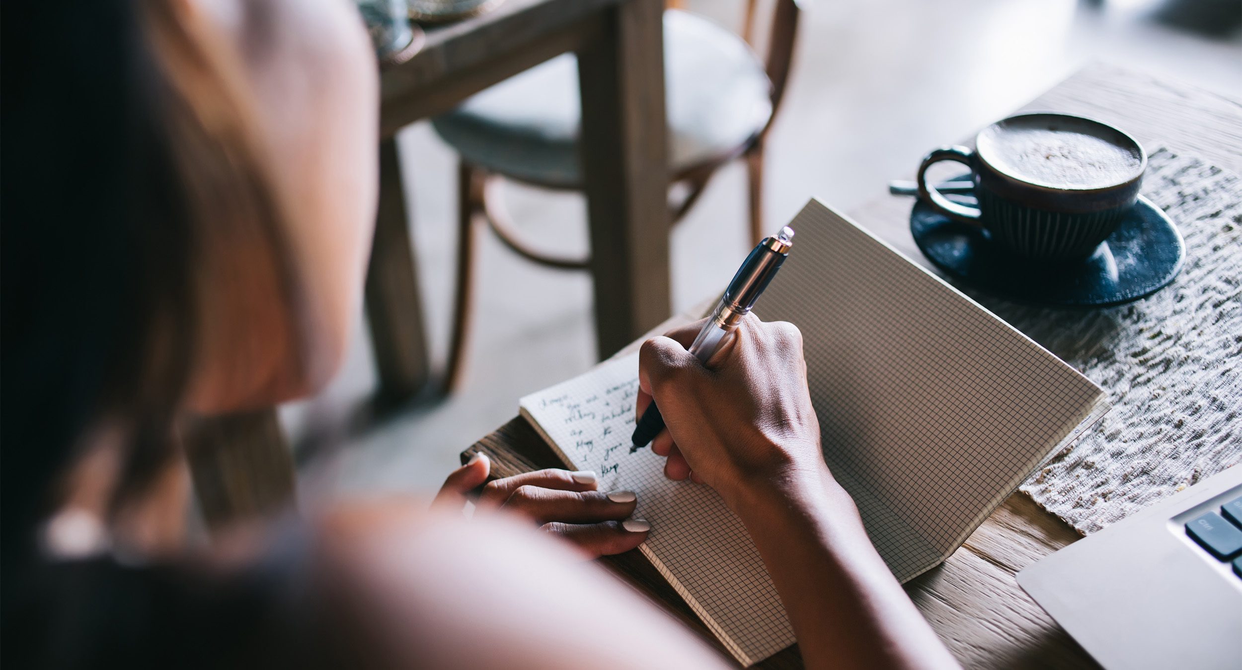 person writing poetry in a journal next to a latte on the table