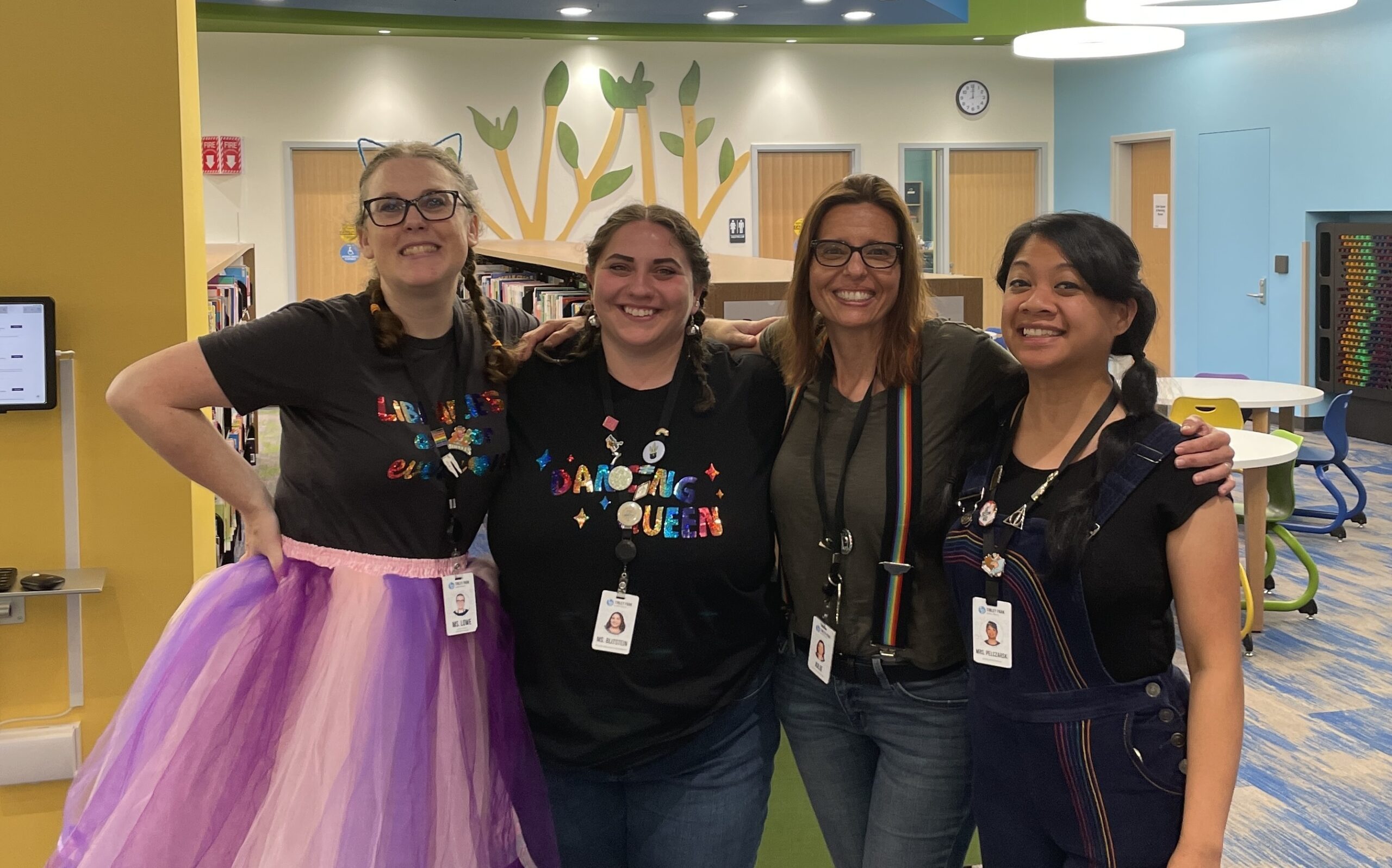 Miss Lowe, Ms. Blitstein, Miss Julie, and Mrs. P. posing in a row with their arms across each other's shoulders and smiling