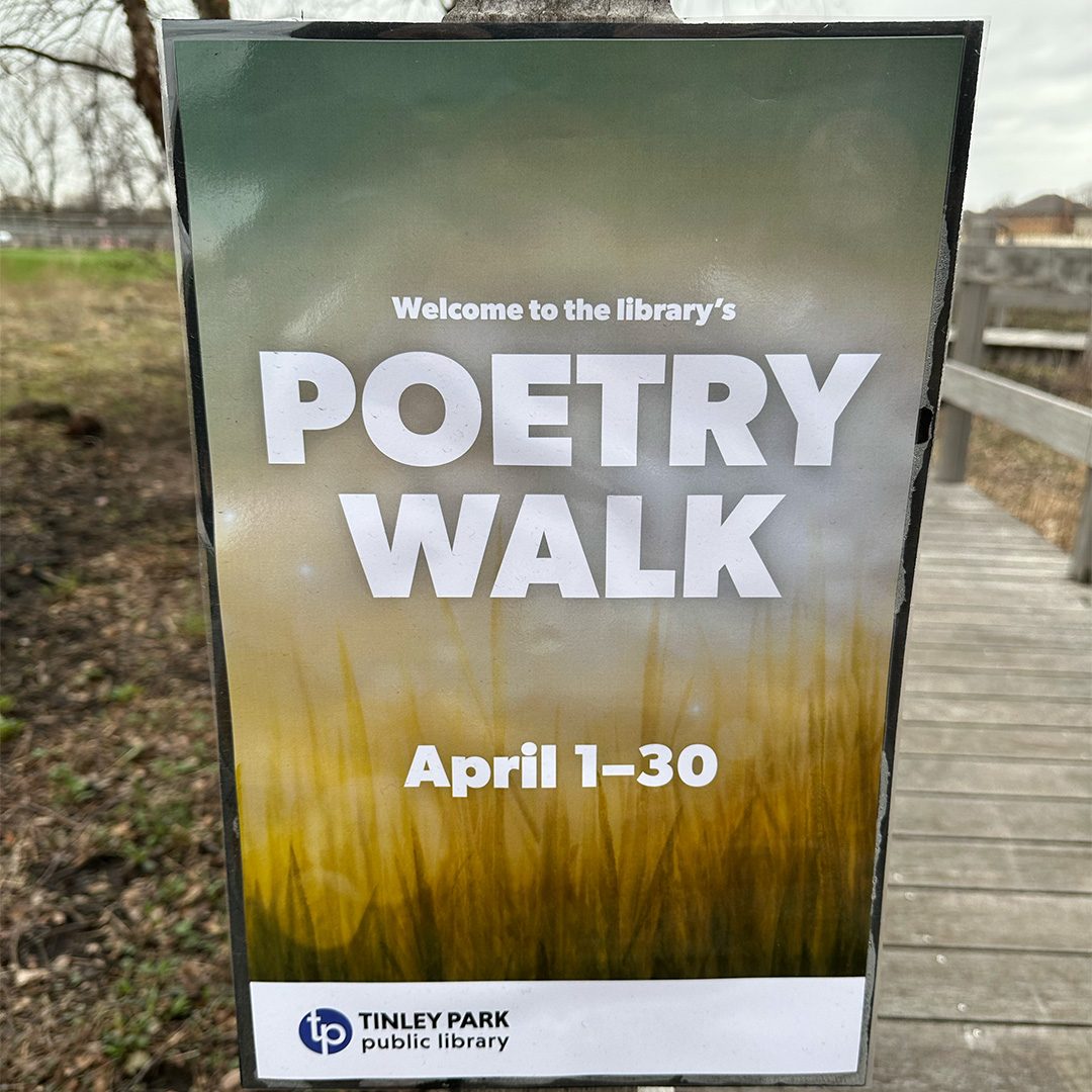 Welcome sign in front of the library boardwalk entry with text that reads Welcome to the library's Poetry Walk April 1–30
