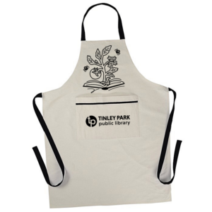 A cream-colored apron with a pocket and black ties, with the Tinley Park Public Library logo on the pocket and an illustration of a book with a tomato plant growing out of it above the pocket