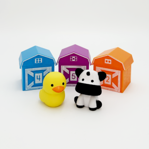 Three toy barns in different colors behind a toy duck and a toy cow