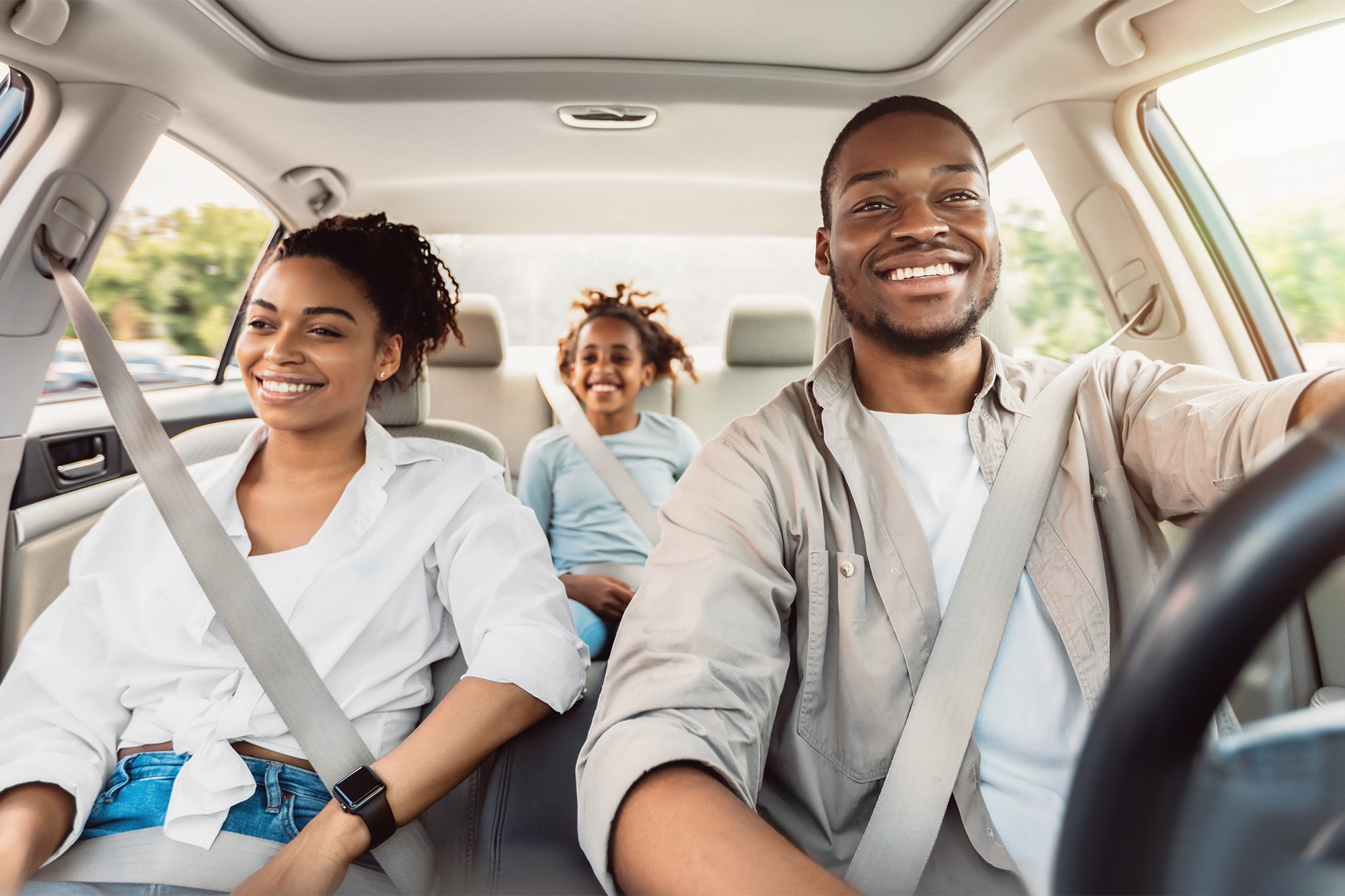 Family of three smiling in a car on a road trip