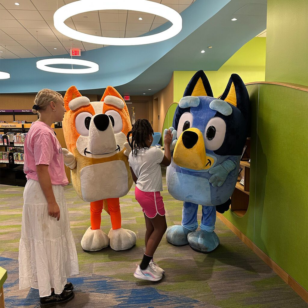 A girl giving a Bluey cosplayer a high five, next to a Bingo cosplayer and a staff member