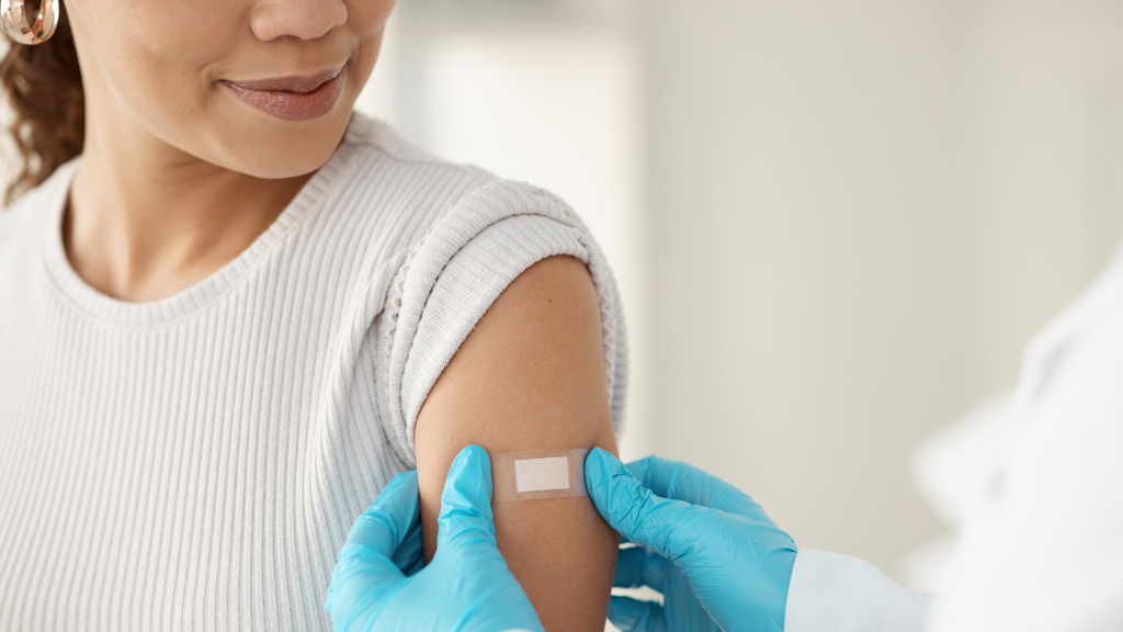 Woman looking down at upper arm as a doctor places a bandaid on it